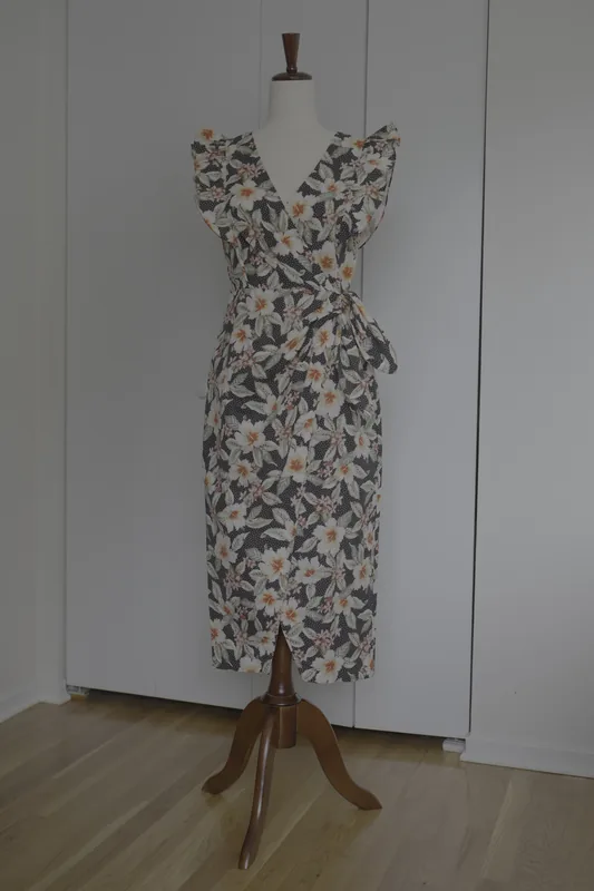 The original photo: a dark dress with white flowers on a dress form, against a gray wall and a white door, on a wooden floor.