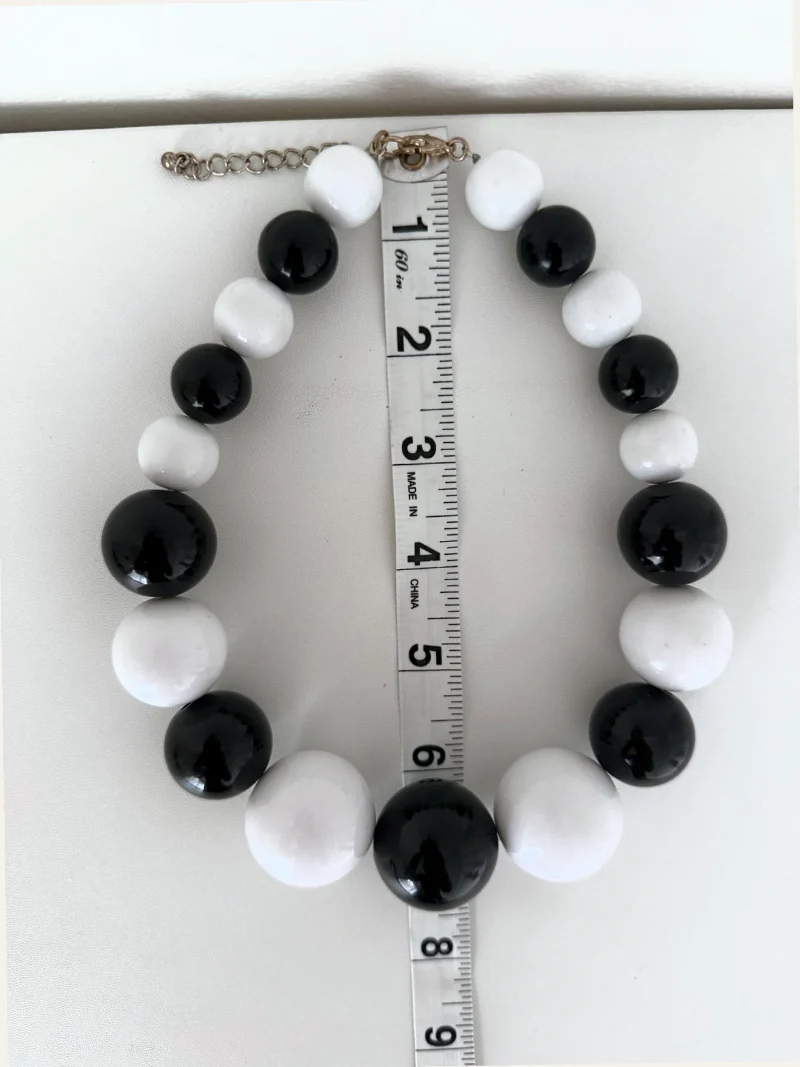 A real photo: a black-and-white bead necklace laid in a circle around a tape measure, slightly tilted.
